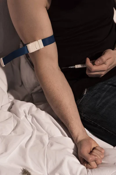 Addict man making injection of heroin while sitting on bedding — Stock Photo