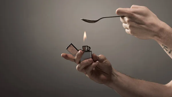 Обрезанный вид на наркомана нагрева ложки с героином на зажигалке на сером фоне — стоковое фото