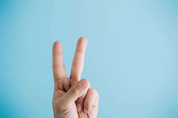 Cropped view of fingers showing peace symbol isolated on blue — Stock Photo