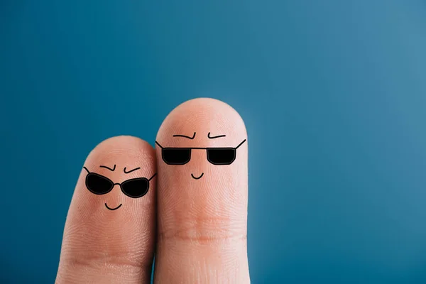 Vista recortada de los dedos sonrientes en gafas de sol aisladas en azul - foto de stock