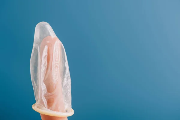 Vista parziale del dito con preservativo isolato sul blu, concetto di contraccezione — Foto stock