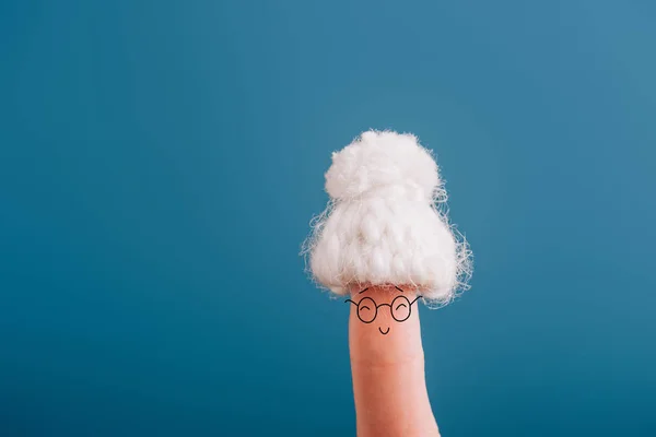 Cropped view of finger as cheerful senior woman in knitted hat isolated on blue — Stock Photo