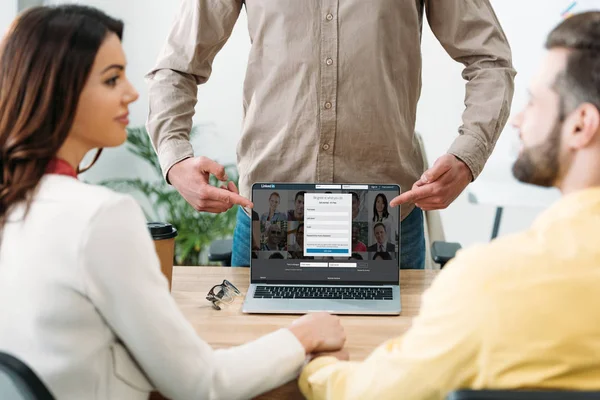 Selective focus of advisor pointing with fingers at laptop with linkedin website on screen near couple in office — Stock Photo