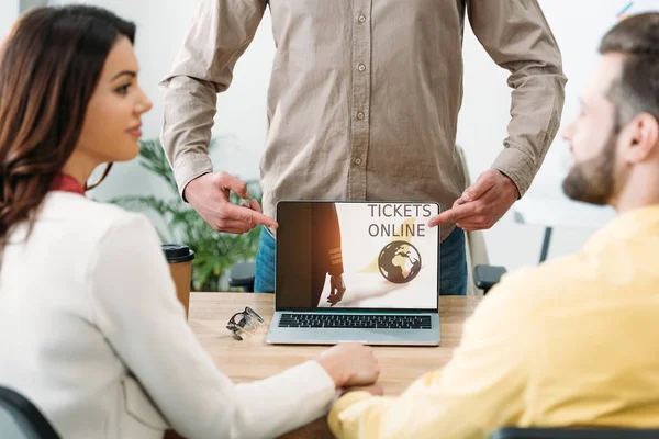 Selective focus of advisor pointing with fingers at laptop with tickets online website on screen to couple in office — Stock Photo