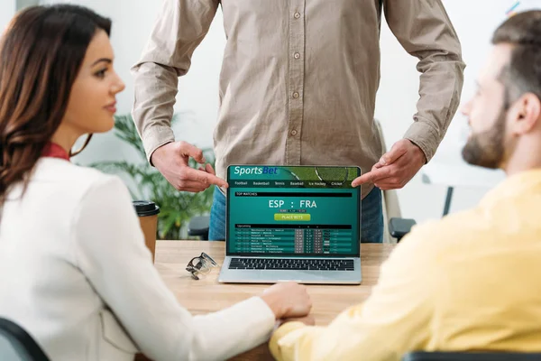 Foco seletivo de conselheiro apontando com os dedos para laptop com site online sportsbet na tela para casal no escritório — Fotografia de Stock