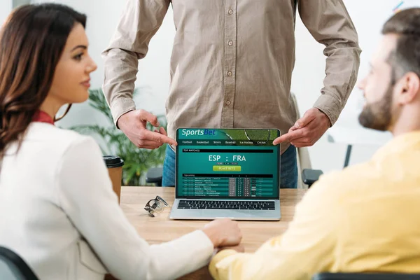 Foyer sélectif du conseiller pointant avec les doigts à l'ordinateur portable avec le site en ligne de paris sportifs à l'écran pour couple dans le bureau — Photo de stock