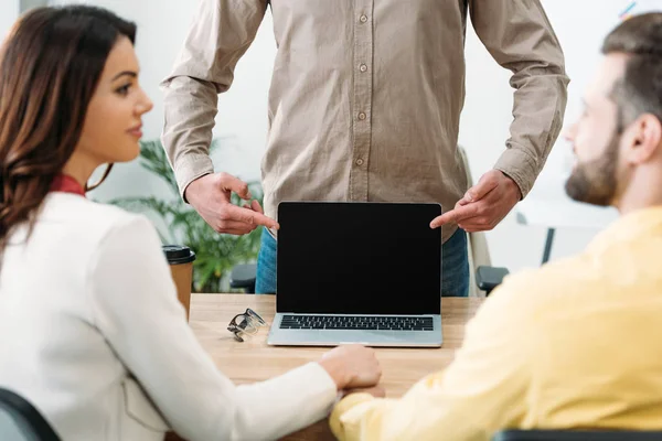 Foco seletivo de conselheiro apontando com os dedos para laptop com tela em branco para casal no escritório — Fotografia de Stock