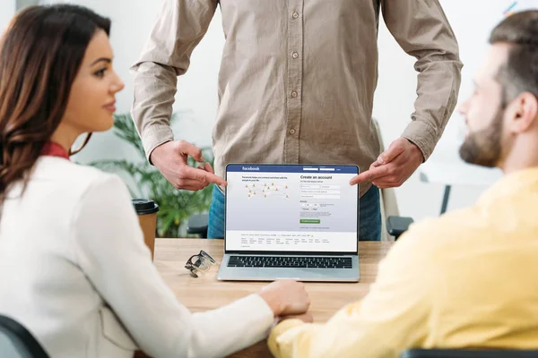 Selektiver Fokus des Beraters zeigt mit dem Finger auf Laptop mit Facebook-Website auf dem Bildschirm auf Paar im Büro — Stockfoto