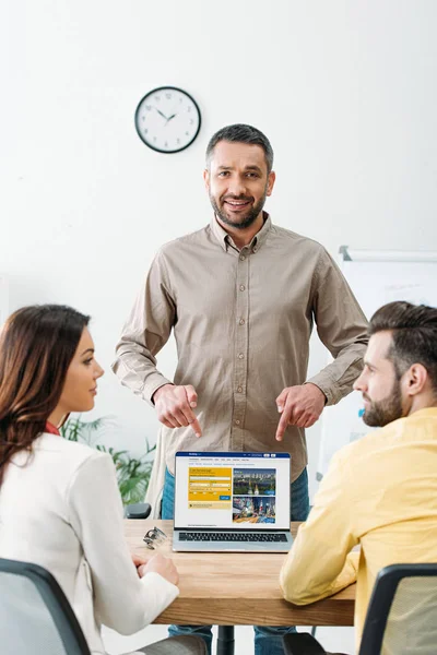 Conseiller pointant avec les doigts à l'ordinateur portable avec le site de réservation à l'écran pour l'homme et la femme au bureau — Photo de stock