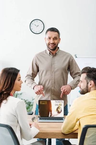 Advisor pointing with fingers at laptop with tickets online website on screen to man and woman in office — Stock Photo