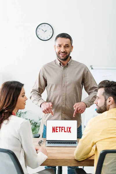 Advisor pointing with fingers at laptop with netflix website on screen to investors in office — Stock Photo