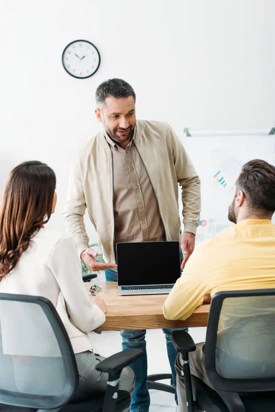 Asesor apuntando con la mano a la computadora portátil con pantalla en blanco a los inversores en la oficina — Stock Photo