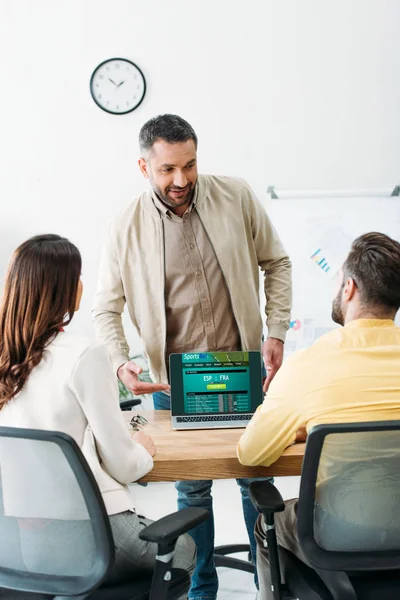 Foyer sélectif du conseiller pointant avec les doigts à l'ordinateur portable avec le site en ligne de paris sportifs à l'écran pour couple dans le bureau — Photo de stock