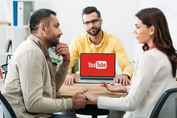 Selective focus of man and woman holding hands near advisor and laptop with youtube website on screen in office — Stock Photo