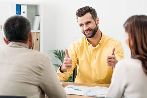 Selektiver Fokus des Beraters am Tisch und Daumendrücken in der Nähe von Mann und Frau im Amt — Stockfoto