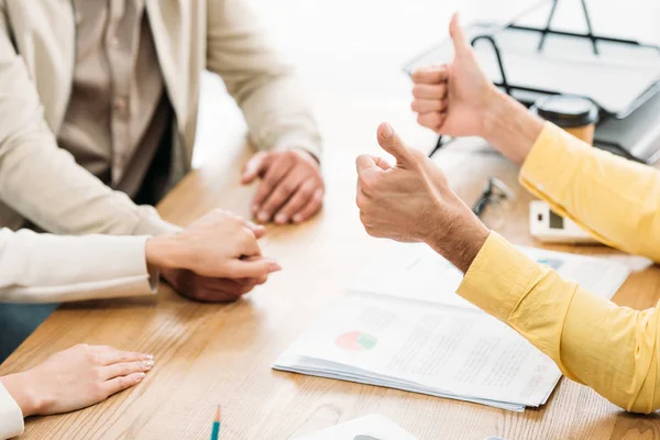 Cropped wiew of advisor sitting at table and thumbing ups near couple in office — Stock Photo