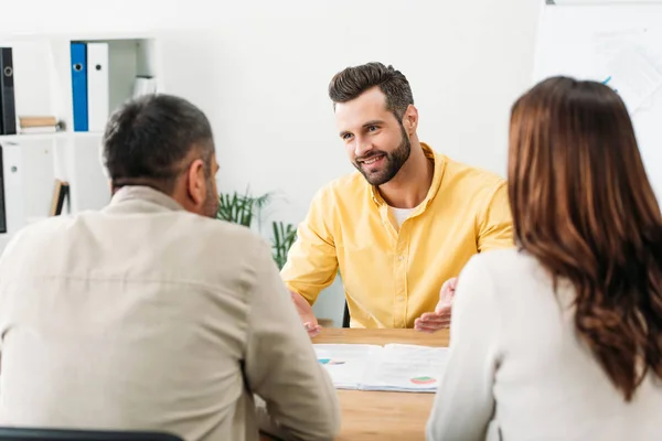 Foco seletivo do consultor sentado à mesa e sorrindo para os investidores no cargo — Fotografia de Stock