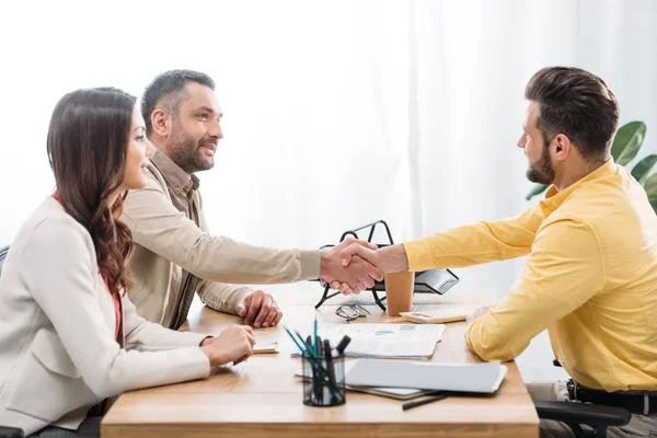 Femme assise à la table wile conseiller et investisseur serrant la main sur la table dans le bureau — Photo de stock