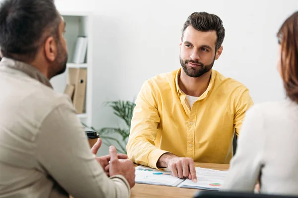 Selektiver Fokus des Beraters, der in der Nähe von Investoren am Tisch sitzt und mit dem Finger auf Dokumente im Büro zeigt — Stockfoto