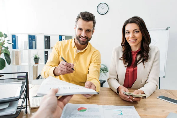 Selektiver Fokus von Frau mit Dollarnoten und Mann mit Stift in der Nähe von Berater, der Dokument im Amt hält — Stockfoto