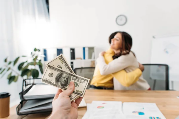 Selective focus of advisor at table holding dollar banknotes wile investors hugging in office — Stock Photo