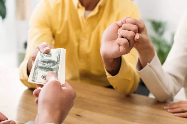 Vista recortada del asesor que da billetes en dólares a los inversores en la mesa en el cargo - foto de stock