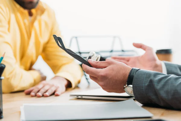 Cropped view of advisor sitting with laptop at table and holding glasses near investor in office — Stock Photo