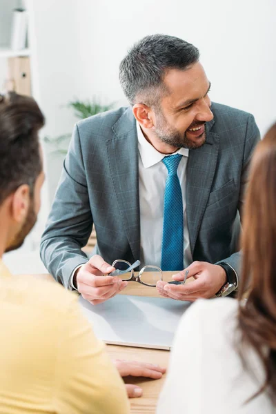 Advisor smiling, sitting at table and holding glasses with investors in office — Stock Photo