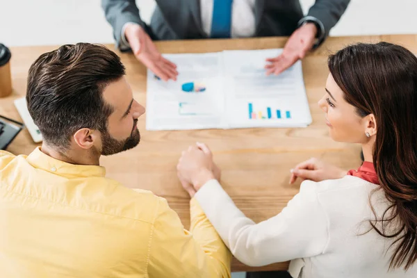 Selektiver Fokus der Investoren, die am Tisch sitzen und Händchen halten, während der Berater Dokumente im Amt zeigt — Stockfoto