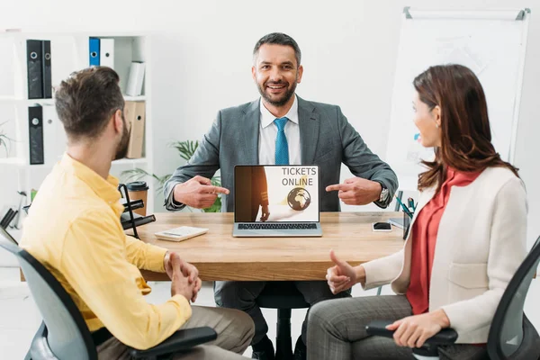 Advisor pointing with fingers at laptop with tickets online website on screen wile man and woman thumbing up in office — Stock Photo