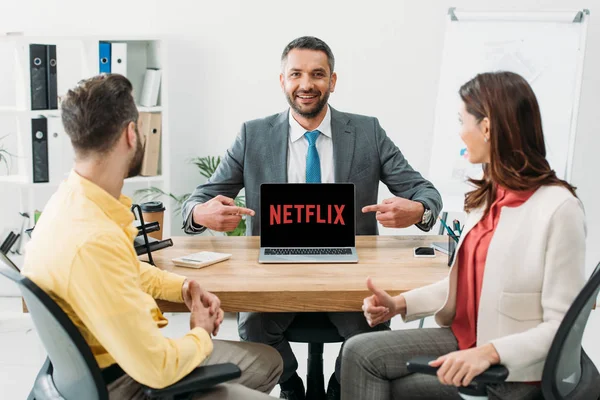 Conseiller pointant avec les doigts à l'ordinateur portable avec netflix site Web à l'écran près de l'homme et la femme pouce vers le haut dans le bureau — Photo de stock