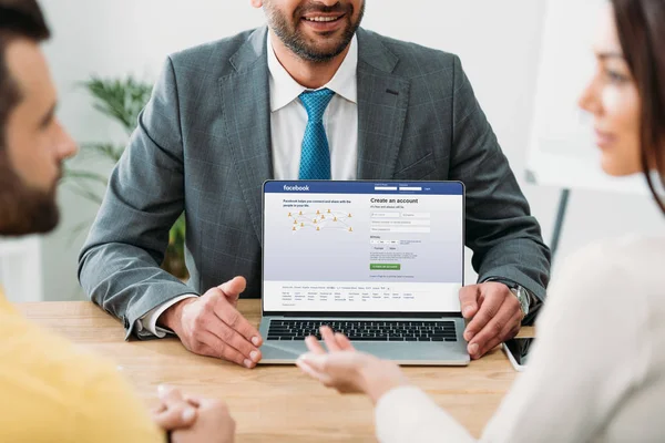 Ausgeschnittene Ansicht des Beraters am Tisch und Laptop mit Facebook-Website auf dem Bildschirm mit Investoren im Büro — Stockfoto