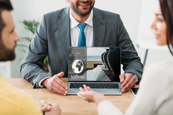 Ausgeschnittene Ansicht des Beraters am Tisch und Laptop mit Buchungswebseite auf dem Bildschirm mit Investoren im Büro — Stockfoto