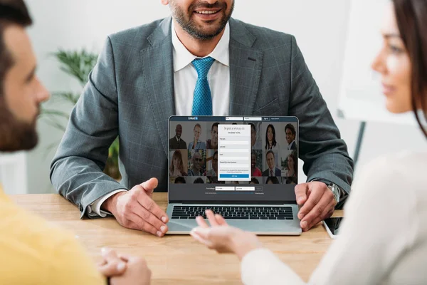 Cropped view of advisor sitting at table and laptop with linkedin website on screen with investors in office — Stock Photo