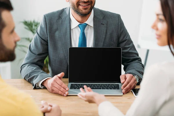 Vista recortada del asesor sentado en la mesa y el ordenador portátil con pantalla en blanco con los inversores en la oficina - foto de stock