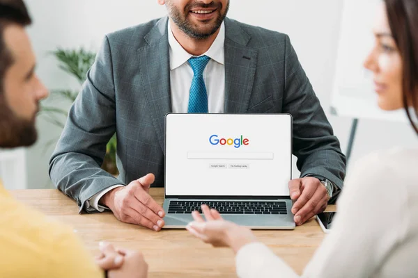 Обрезанный вид советника, сидящего за столом и ноутбуком с веб-сайта Google на экране с инвесторами в офисе — стоковое фото