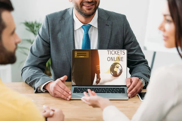 Cropped view of advisor sitting at table and laptop with tickets online website on screen with investors in office — Stock Photo