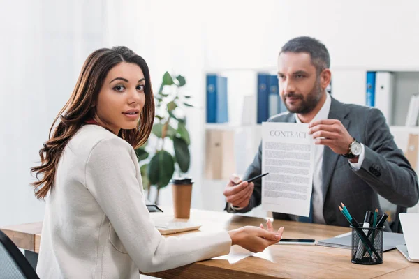 Enfoque selectivo de la mujer sentada en la mesa asesor astuto señalando el contrato con la pluma en la oficina - foto de stock