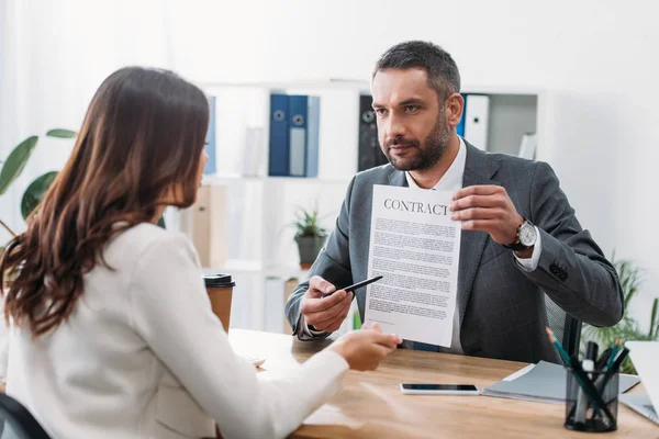 Selektiver Fokus des Beraters, der am Tisch sitzt und auf den Vertrag mit dem Stift zeigt, auf die Frau im Amt — Stockfoto