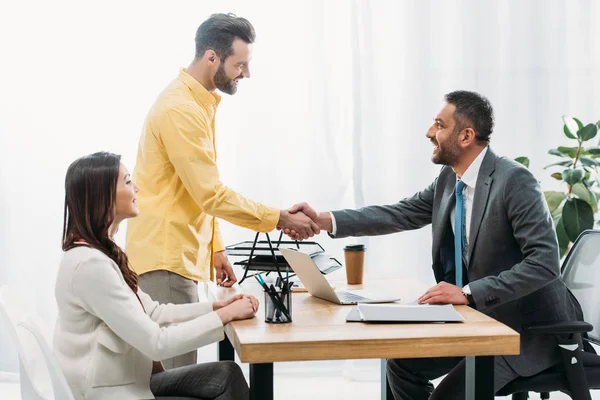 Advisor and investor shaking hands over table wile woman sitting in office — Stock Photo