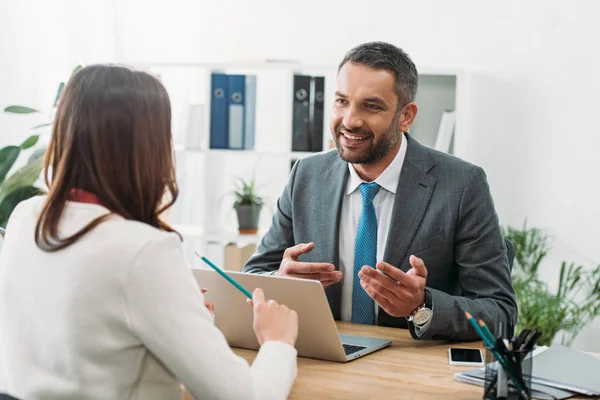 Selective focus of advisor sitting at table with laptop and woman in office — Stock Photo