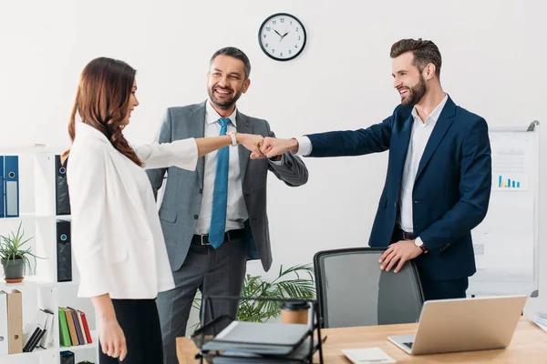 Colleagues standing near table, smiling and celebrating in office — Stock Photo