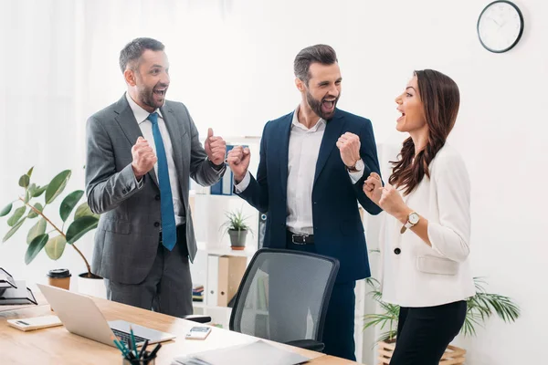 Colegas de pie cerca de la mesa y celebrando en la oficina - foto de stock