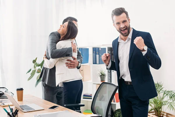 Collègues embrasser, sourire et célébrer près de la table dans le bureau — Photo de stock