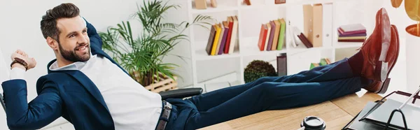 Hombre de negocios sentado con las piernas en la mesa y sonriendo en la oficina - foto de stock