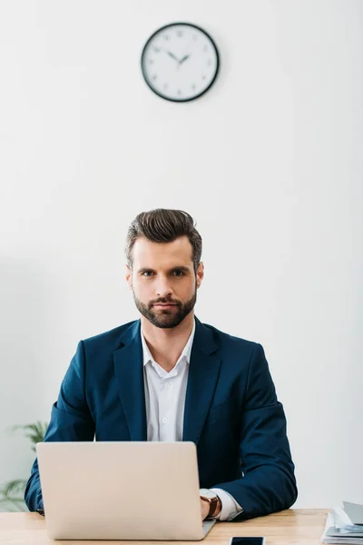 Empresário em terno azul sentado à mesa com laptop no escritório — Fotografia de Stock