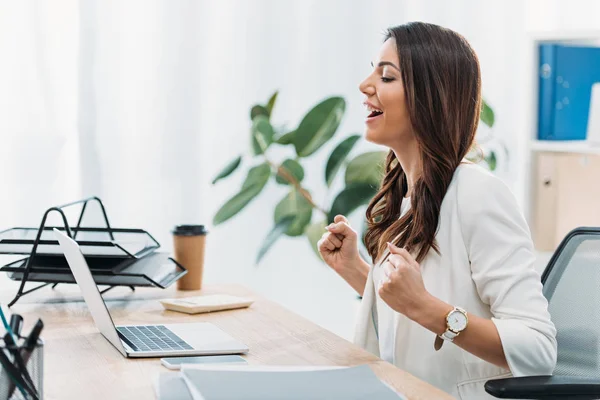 Geschäftsfrau sitzt am Tisch, blickt auf Laptop und freut sich im Büro — Stockfoto