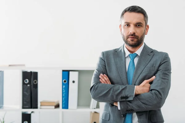 Handsome businessman standing with crossed arms in office — Stock Photo