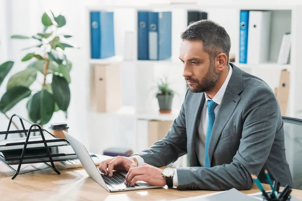 Bell'uomo d'affari seduto a tavola con computer portatile e digitando in ufficio — Foto stock