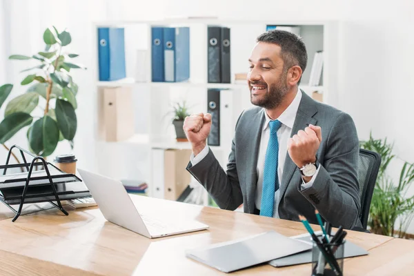Schöner Geschäftsmann sitzt mit Laptop am Tisch und zeigt Ja-Geste im Büro — Stockfoto